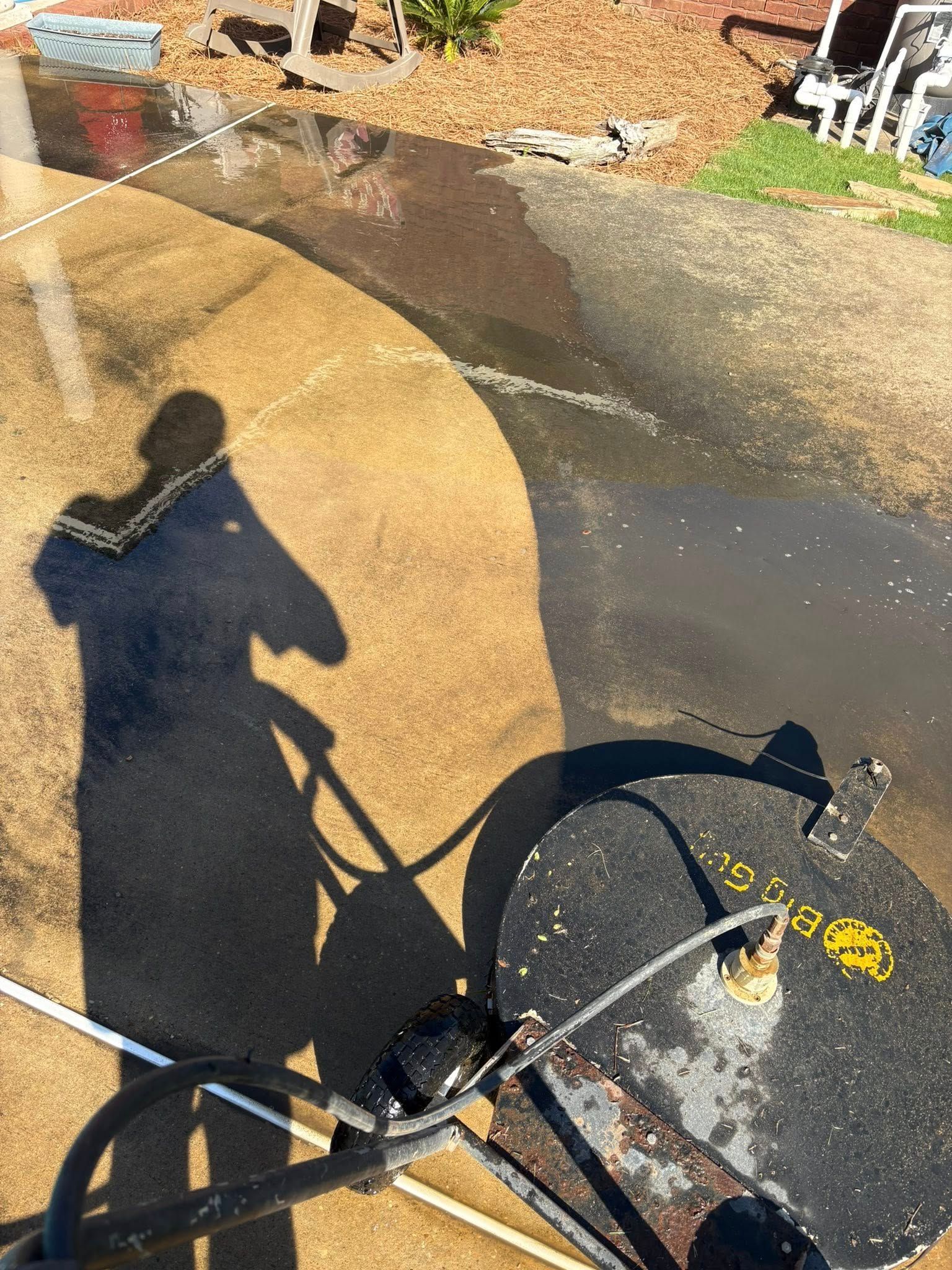 Shadow of person using a pressure washer cleaning a concrete driveway.