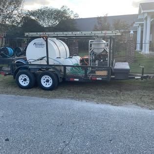 Trailer with tanks, pressure washing equipment, and ladder parked on grass near a house.