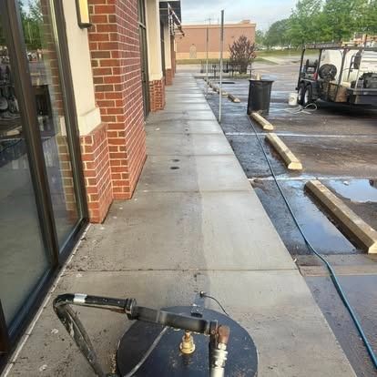 A sidewalk being cleaned with a pressure washer; half is clean, the other half is dirty and stained.