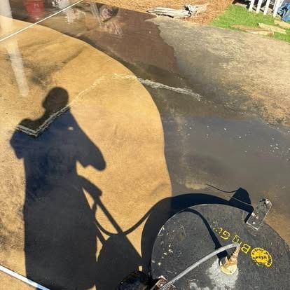 Person pressure washing a concrete surface with a circular cleaner. Shadow visible on the surface.
