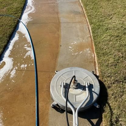 Power washer cleaning a concrete sidewalk, revealing a clean section.