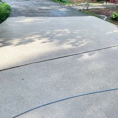 A concrete driveway with a dark stain in the middle and green bushes to the left.