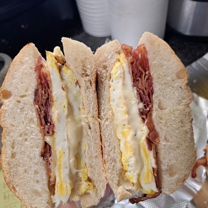 A sandwich with eggs , bacon and cheese is cut in half.