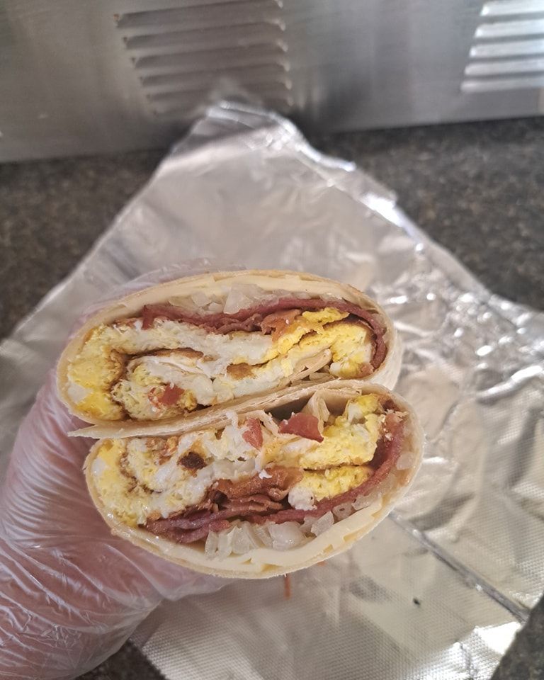 A person is holding a sandwich cut in half on a piece of tin foil.