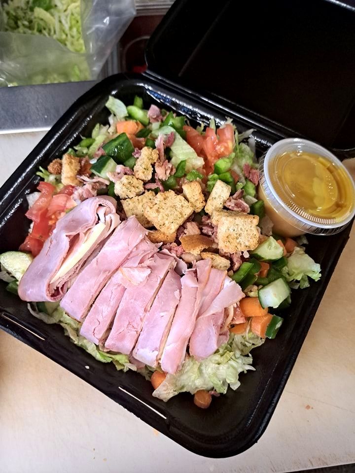 A salad with ham , lettuce , tomatoes and croutons in a plastic container.