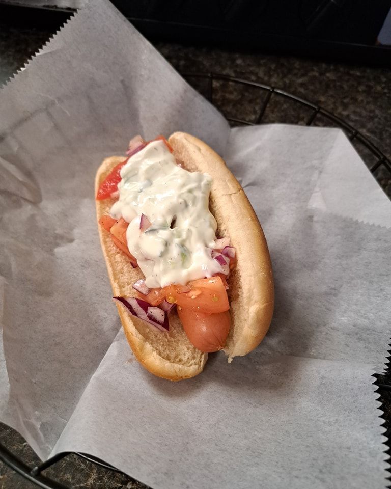 A hot dog with tomatoes , onions and ranch dressing on a bun.