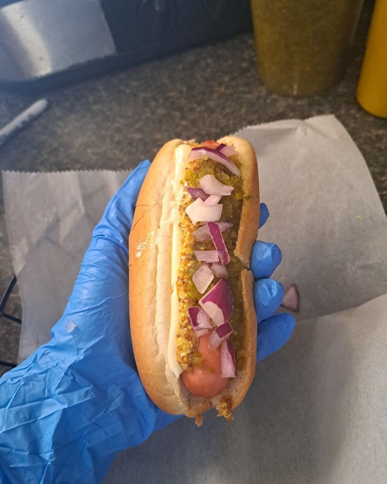 A person wearing blue gloves is holding a hot dog