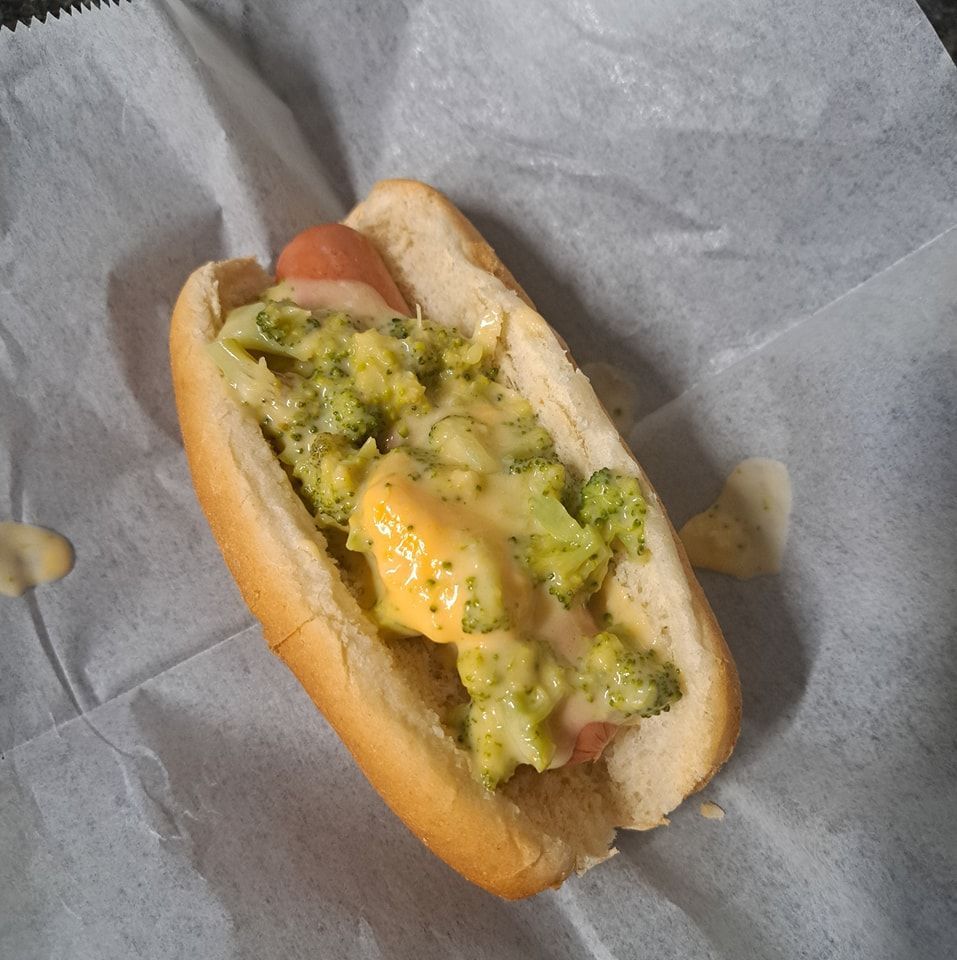 A hot dog with broccoli and cheese on a bun