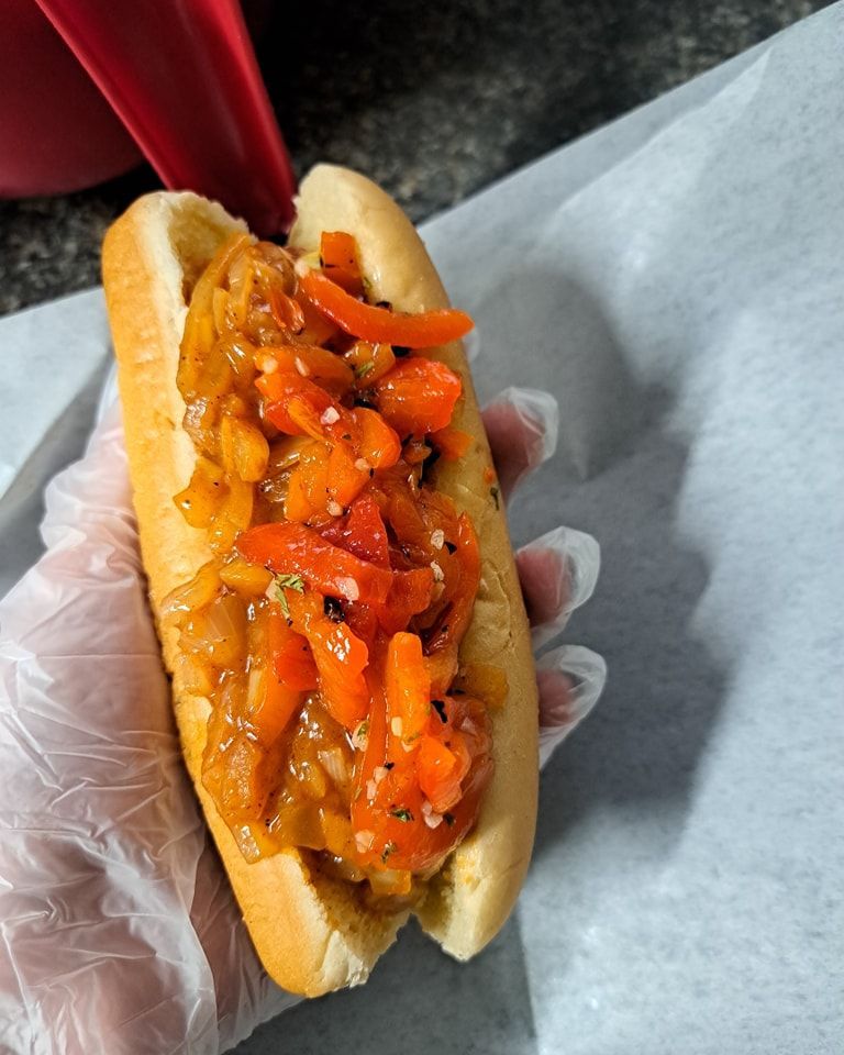 A person is holding a hot dog with carrots and onions on a bun.