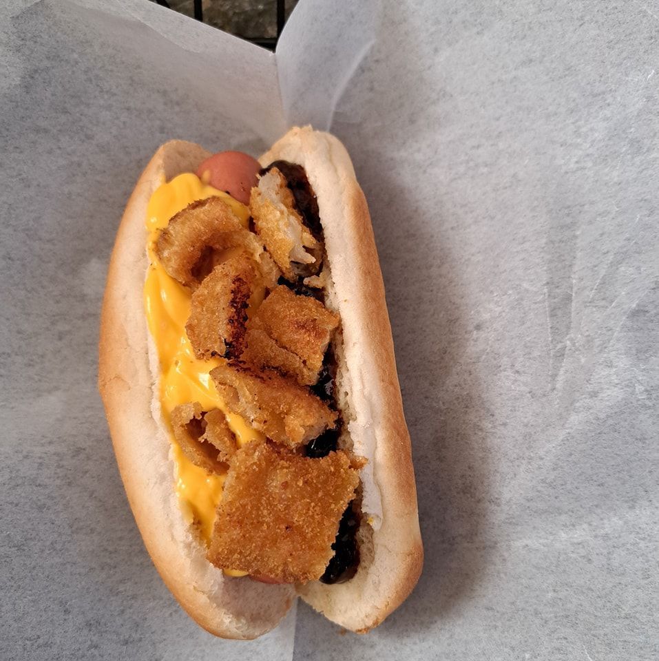 A hot dog with cheese and onion rings on a bun