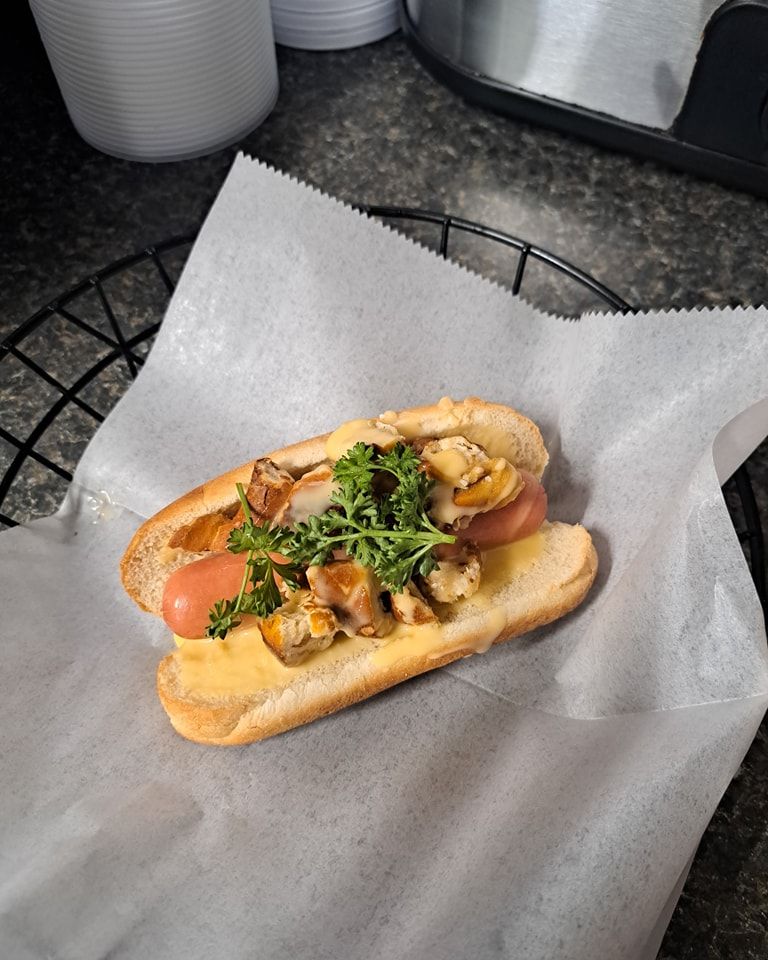 A hot dog with mushrooms and cheese on a bun is sitting on a piece of wax paper.