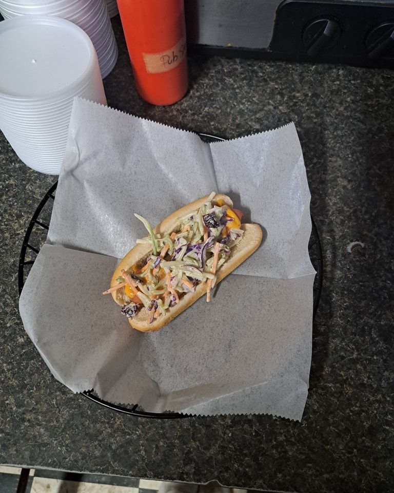 A hot dog with coleslaw on it is sitting on a plate on a counter.