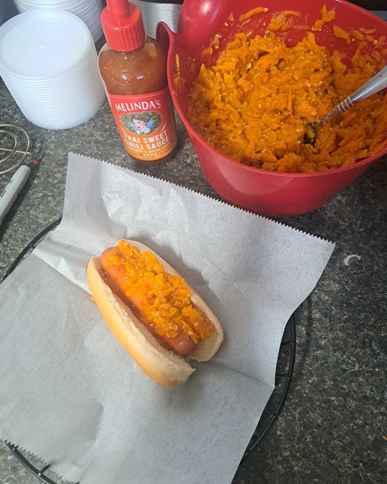A hot dog on a bun next to a bowl of mashed potatoes