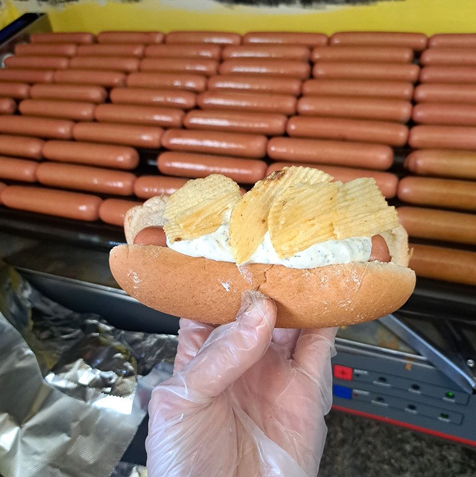 A person is holding a hot dog with potato chips on it
