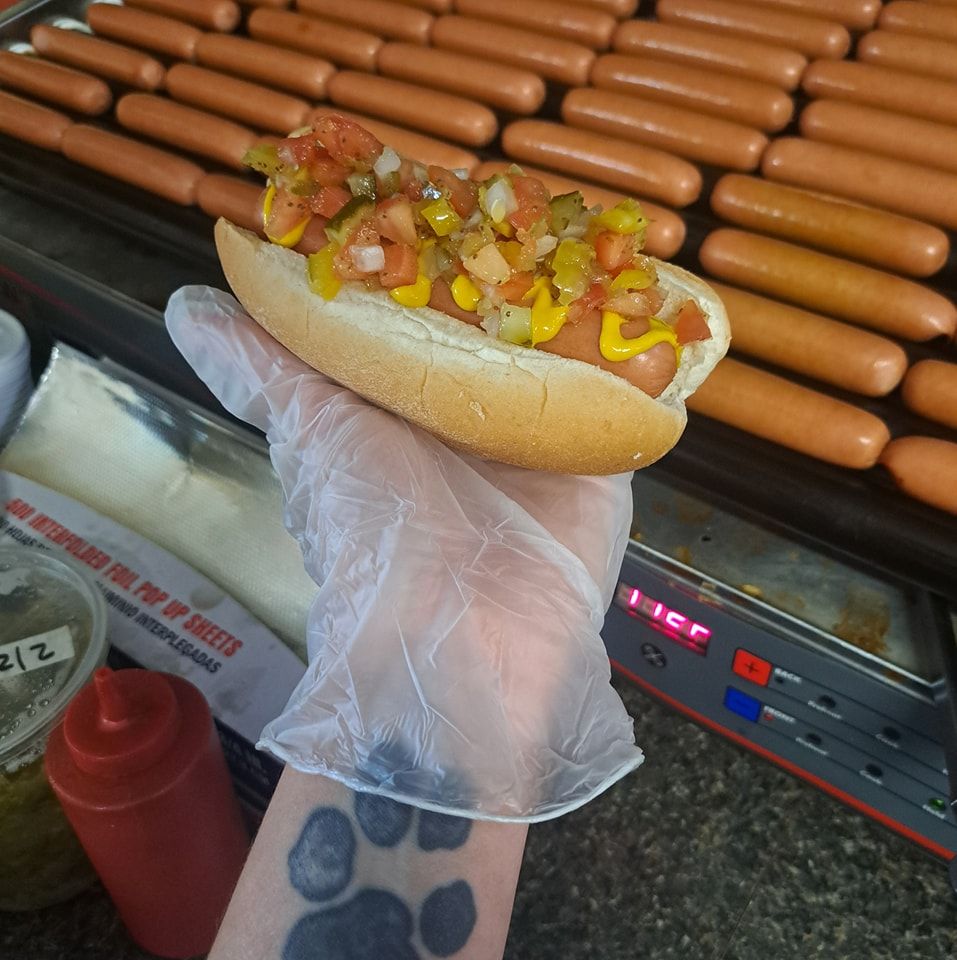 A person holding a hot dog in front of a bunch of hot dogs
