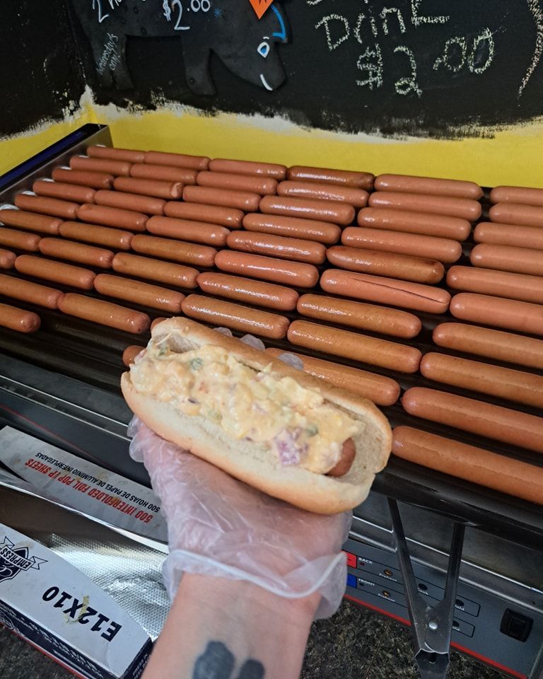A person holding a hot dog in front of a bunch of hot dogs