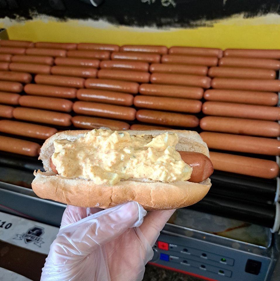 A person is holding a hot dog in front of a bunch of hot dogs