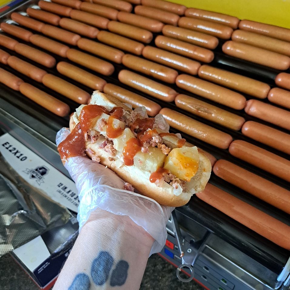 A person holding a hot dog in front of a bunch of hot dogs