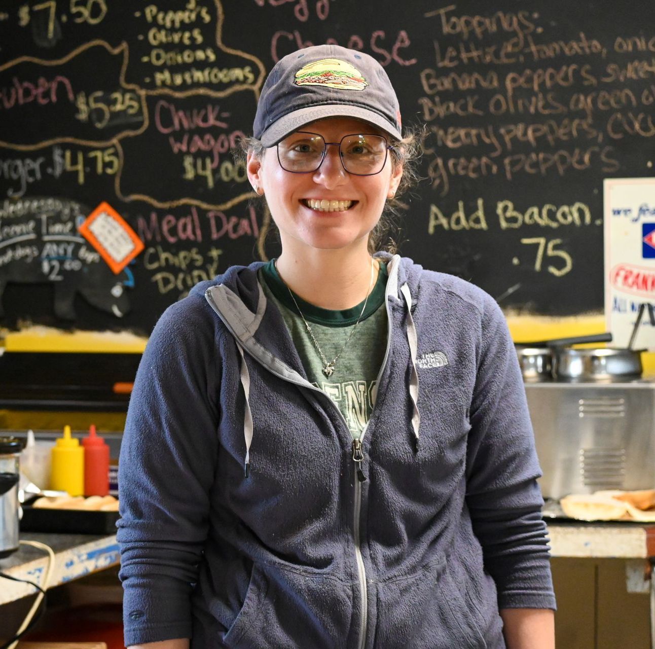 A woman standing in front of a blackboard that says add bacon 75