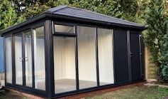 A black shed with lots of windows and doors in a backyard.