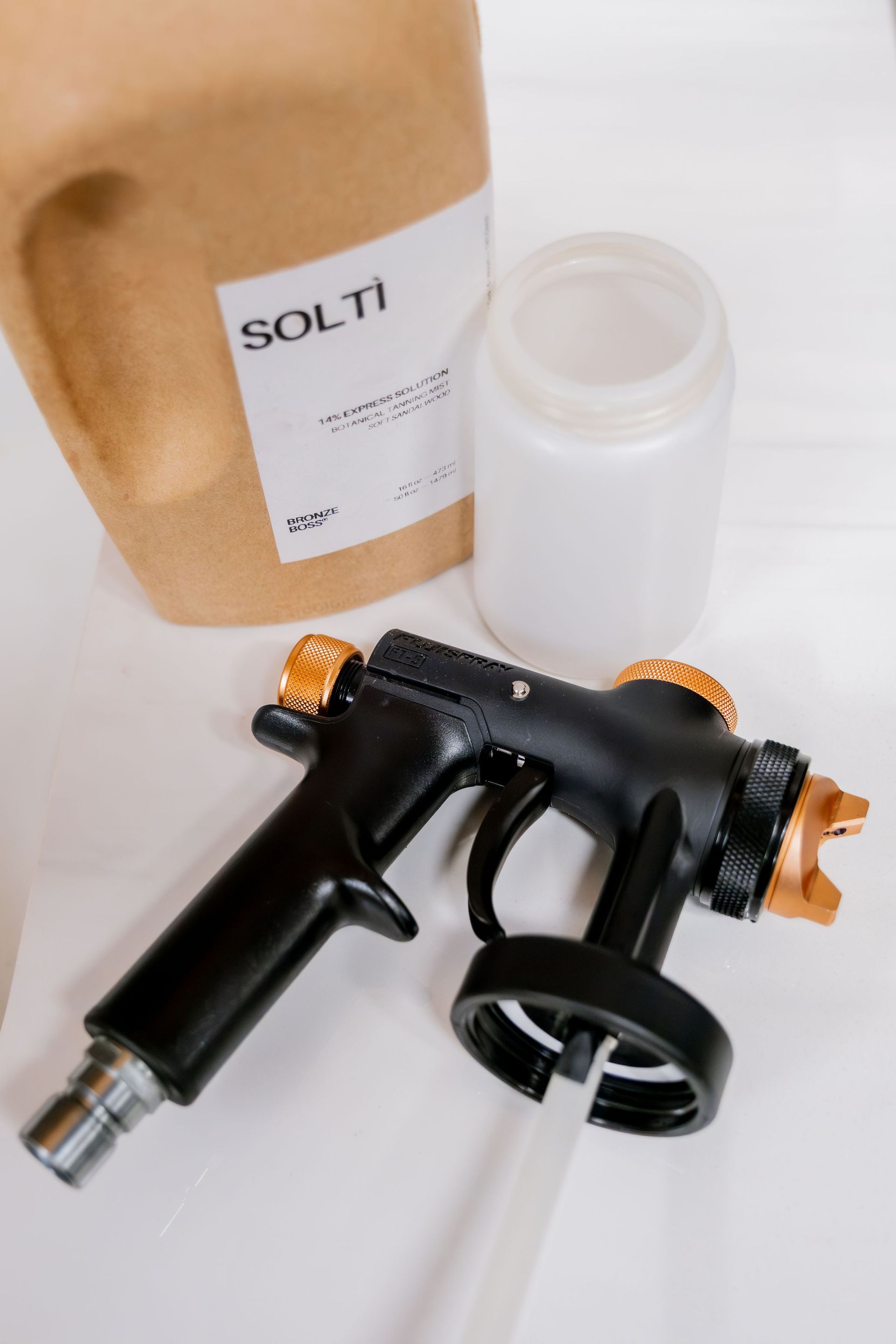 A black spray gun with orange accents, a white plastic container.