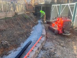 A man is working on a drainage system in a backyard.