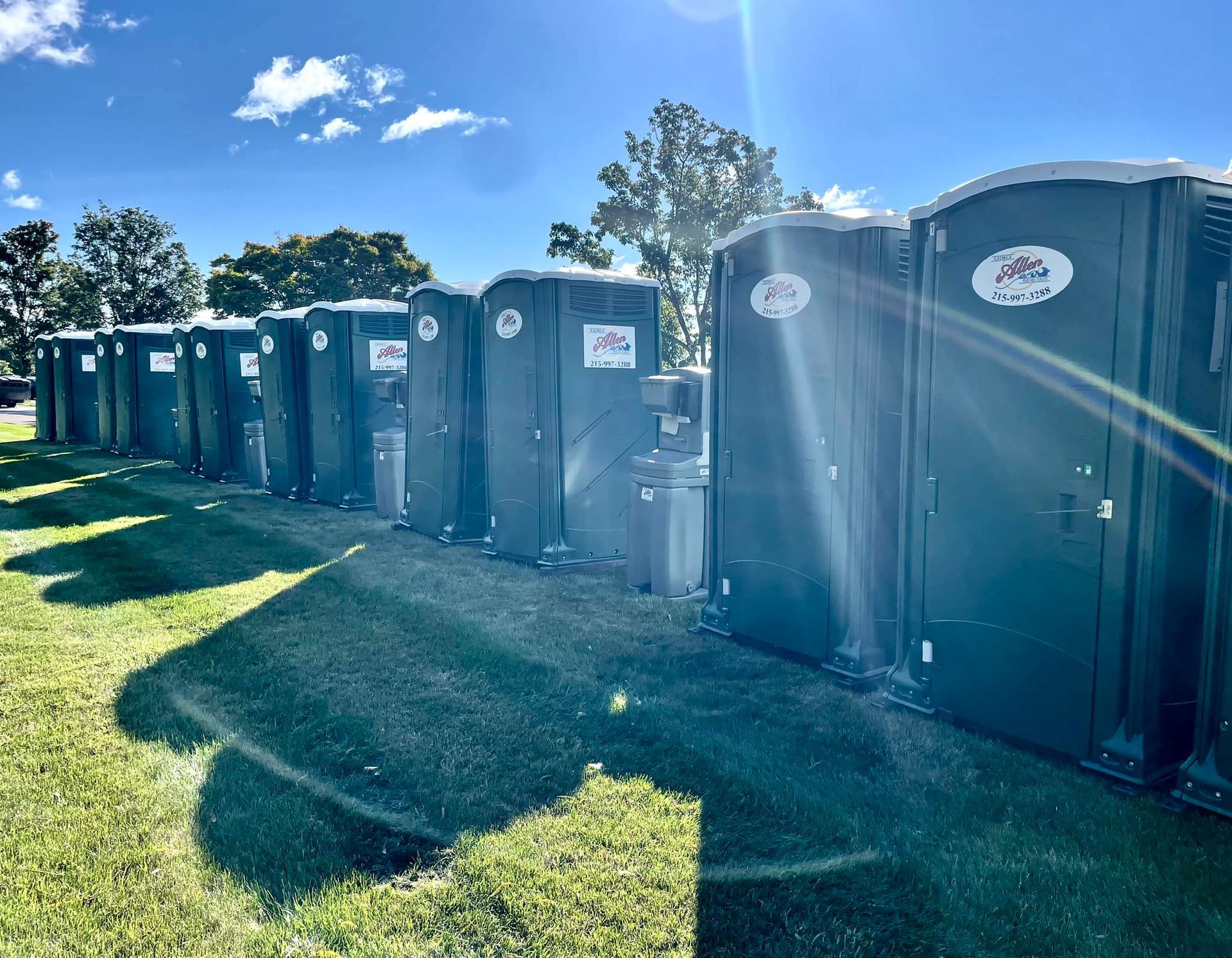 Row of dark green portable toilets lined up on grass.
