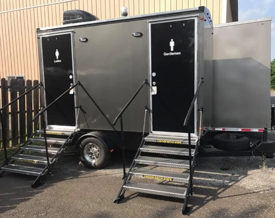 Portable restroom trailer with dual doors, stairs, and gender-marked facilities.