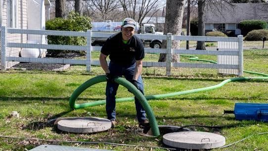 A man is pumping septic tanks with a green hose.
