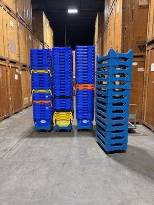 Blue storage containers stacked on dollies, in a warehouse with wooden storage units.