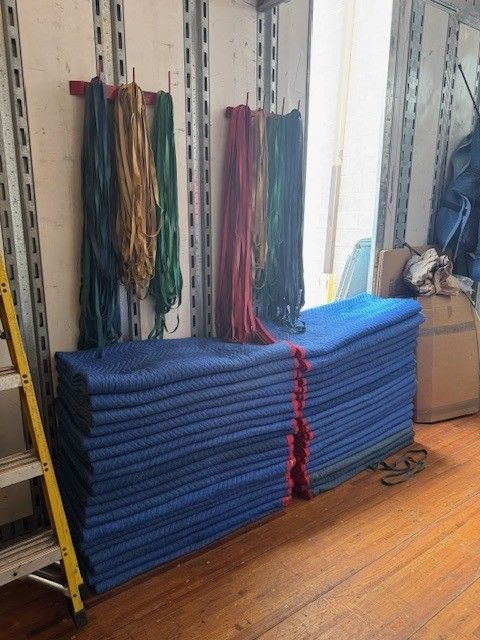 Blue padding stacked near hanging ropes, against a wall with a ladder.