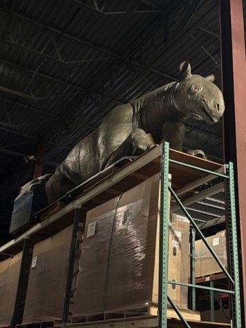 Dinosaur statue atop a warehouse shelf, brown color, indoors.
