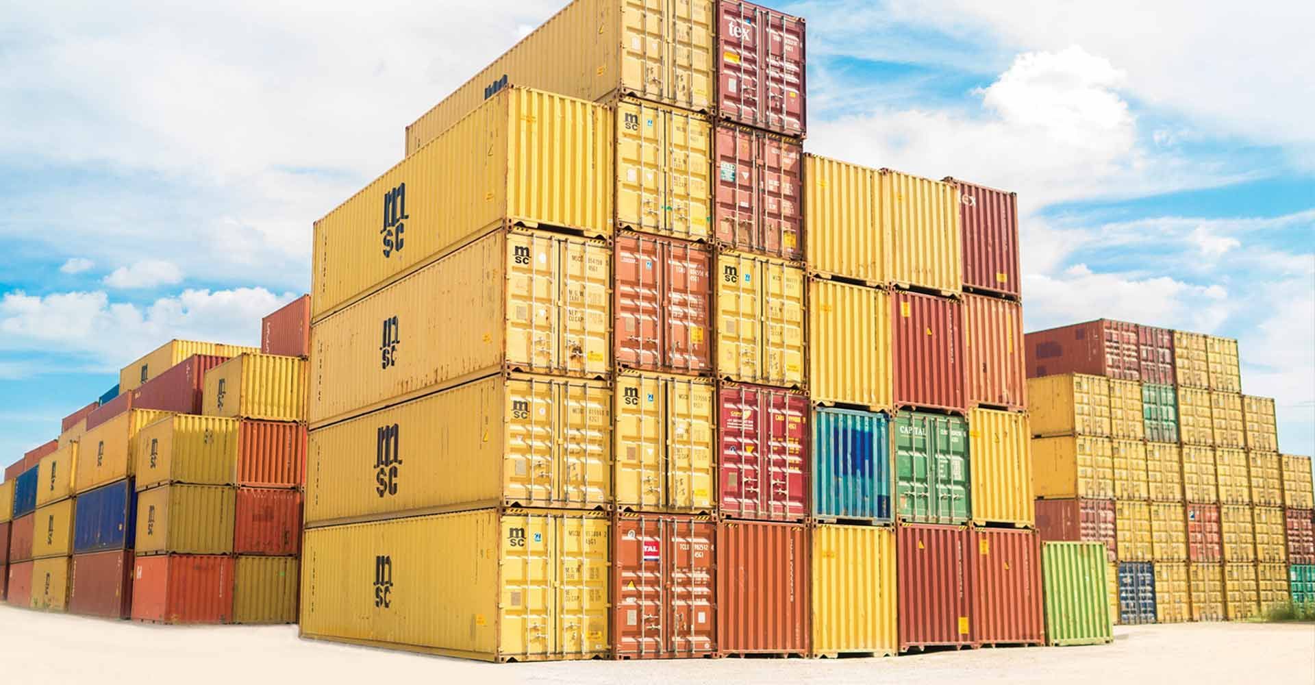 Stacks of colorful shipping containers outdoors against a blue sky.