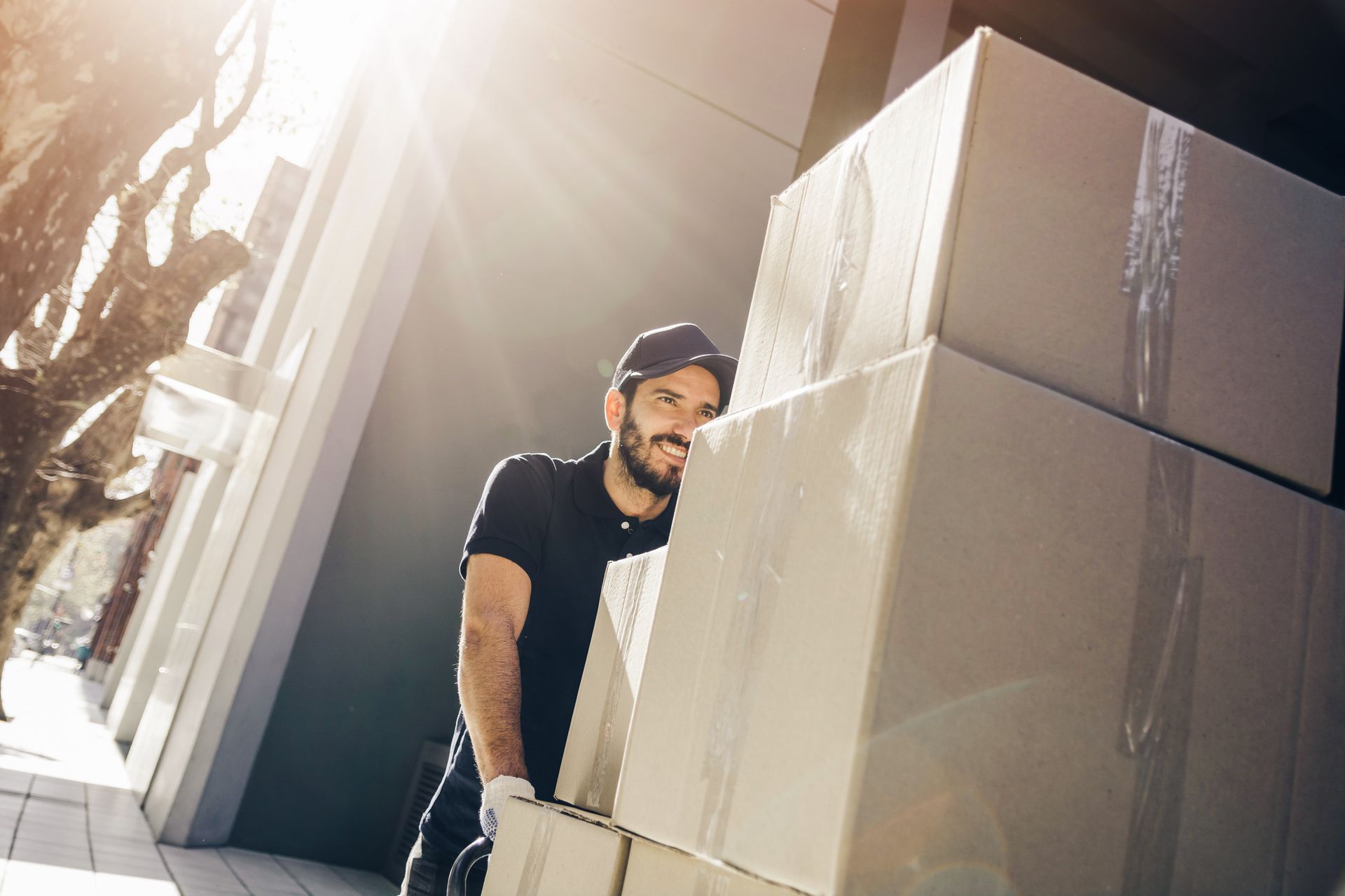 Delivery person carrying stacked cardboard boxes outside a building.