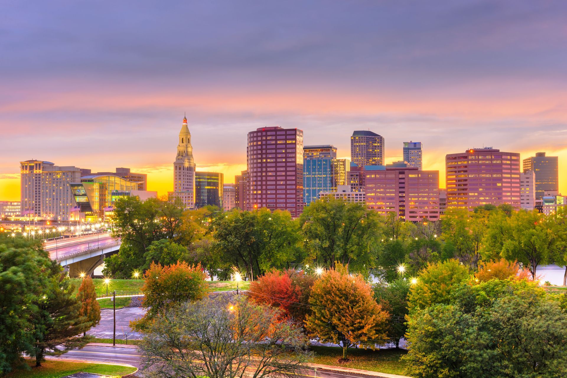 Skyline view of Hartford, Connecticut, with buildings and colorful autumn trees under a sunset.