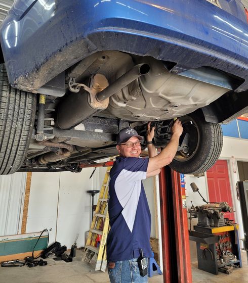 Mechanic working on the underside of a blue car raised on a lift | Mr. Fix It Auto Repair