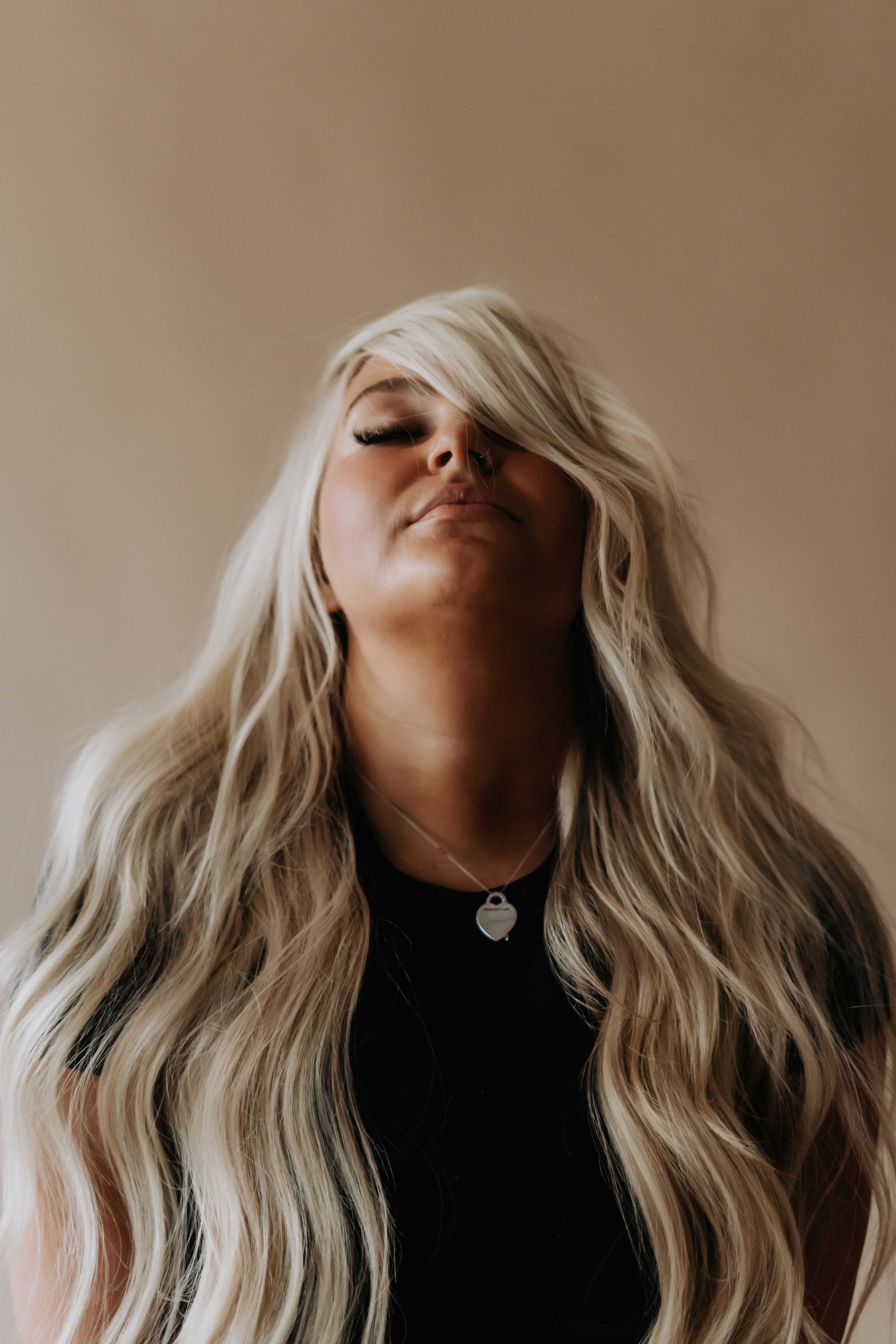 A woman with long blonde hair is looking up with her eyes closed.