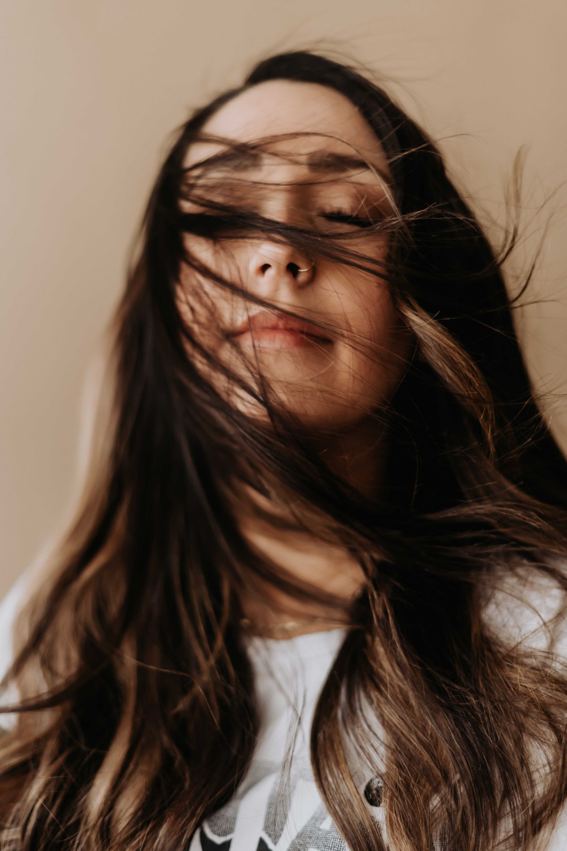 A close up of a woman 's face with her hair blowing in the wind.
