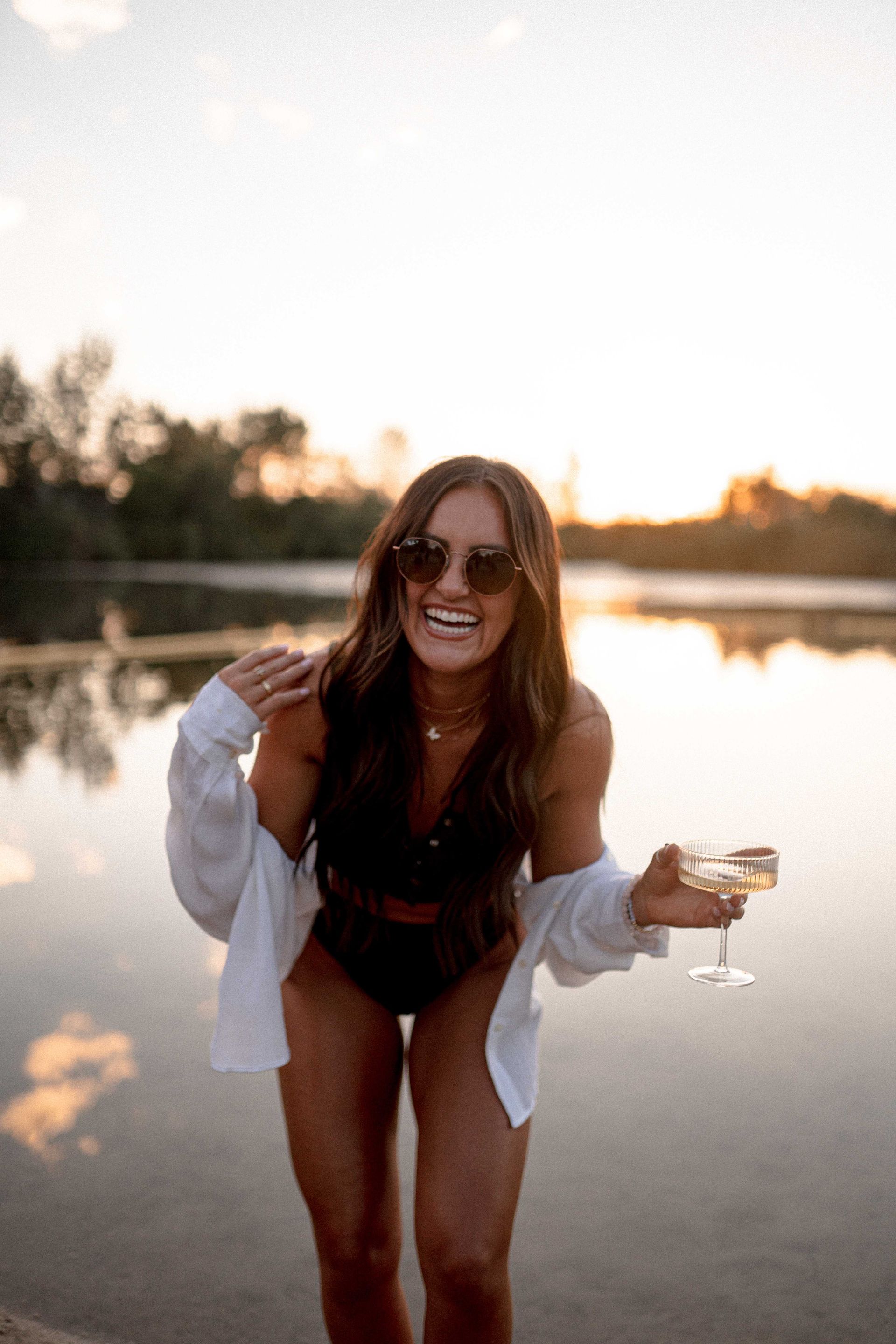 A woman in a bikini is standing in the water holding a glass of champagne.