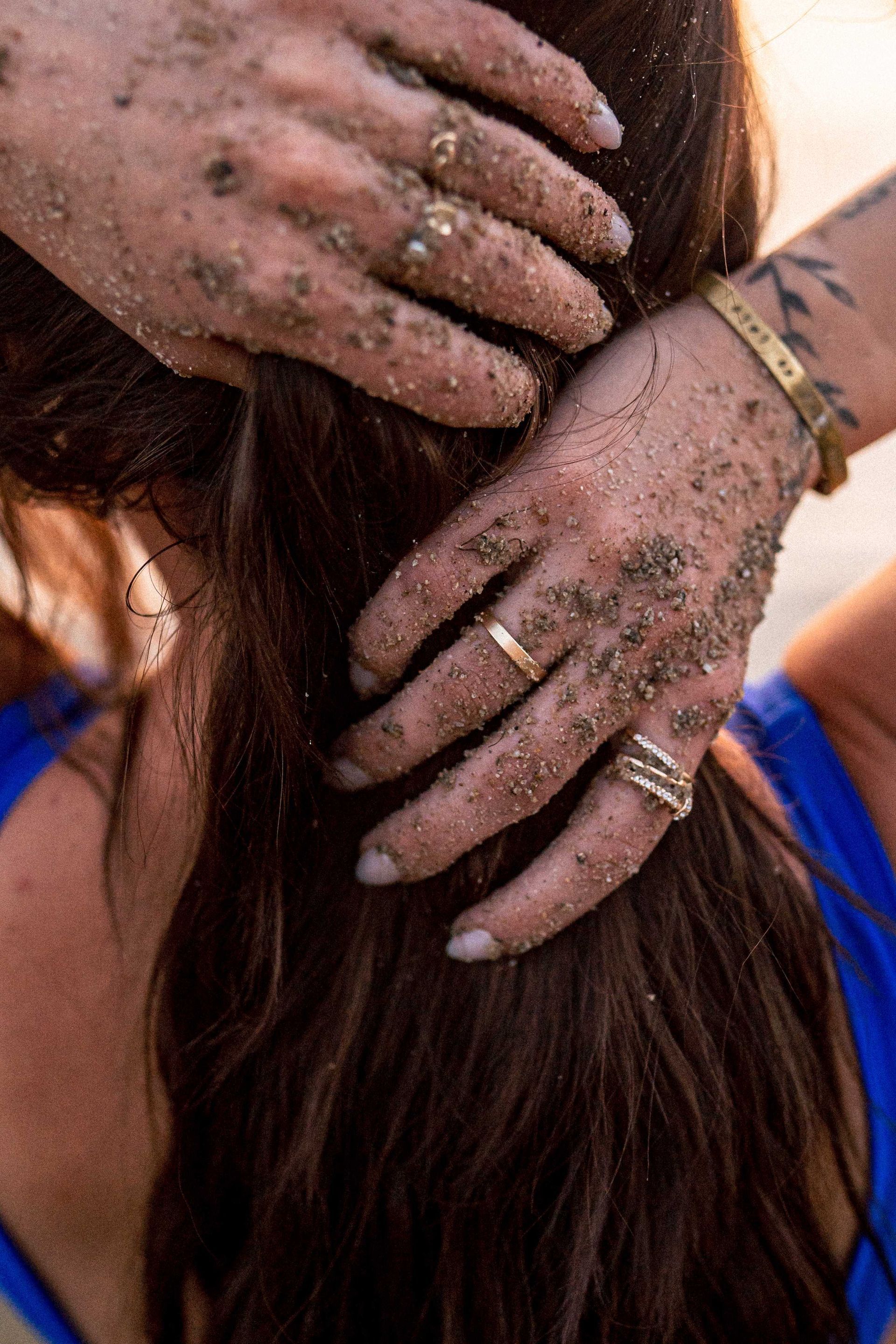 A woman is holding her hair with her hands covered in sand.