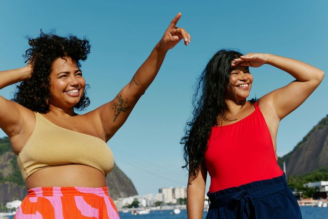 Two women are standing next to each other in front of a body of water.