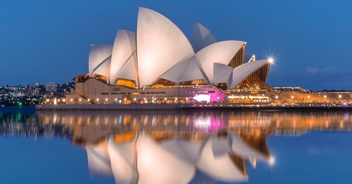 The sydney opera house is lit up at night and reflected in the water.