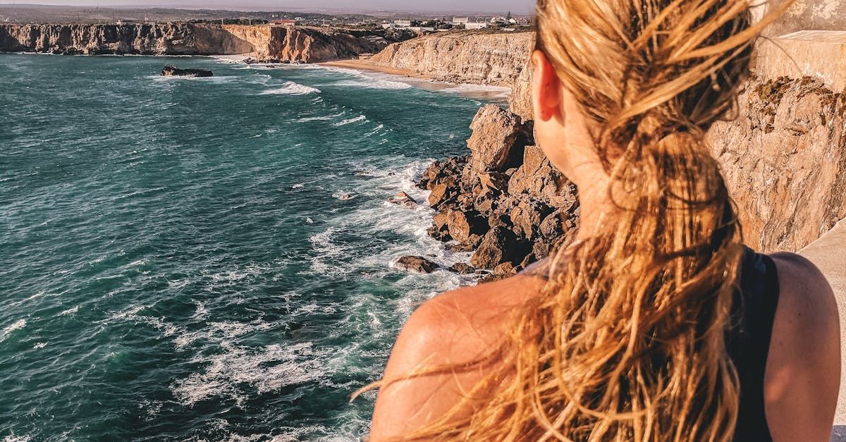 A woman is standing on a cliff overlooking the ocean.
