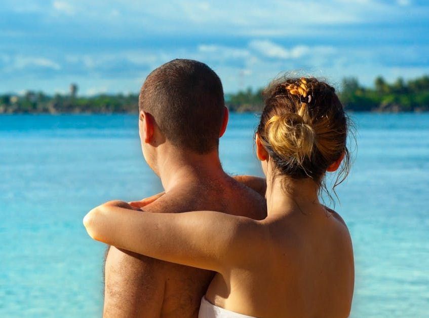 A man and a woman are standing on a beach looking at the ocean.