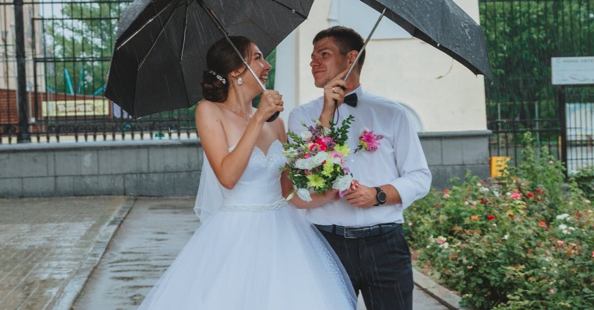 A bride and groom are standing under an umbrella in the rain.