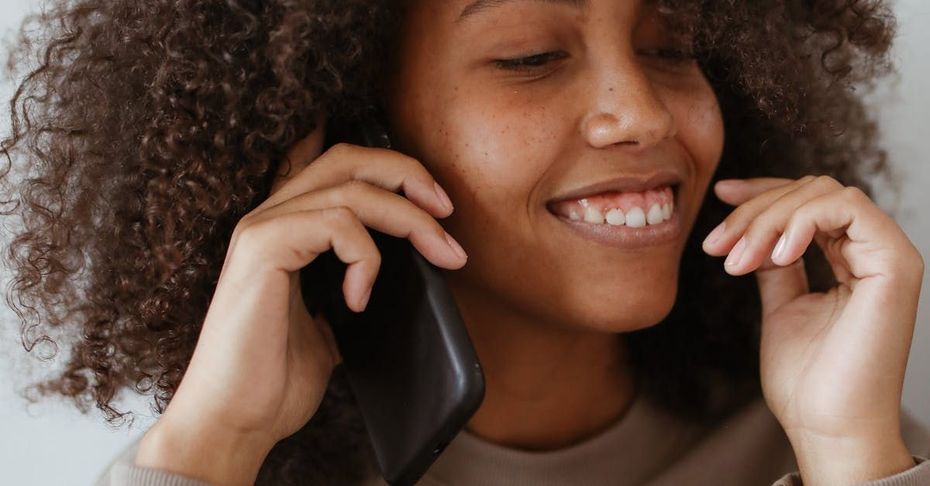 A woman is smiling while talking on a cell phone.
