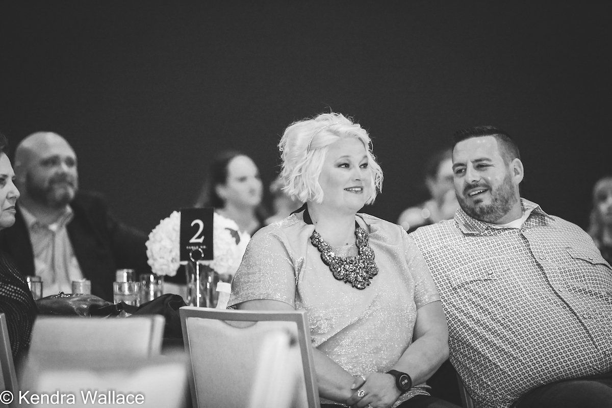 Woman with blonde hair and man in a patterned shirt smiling at an event.