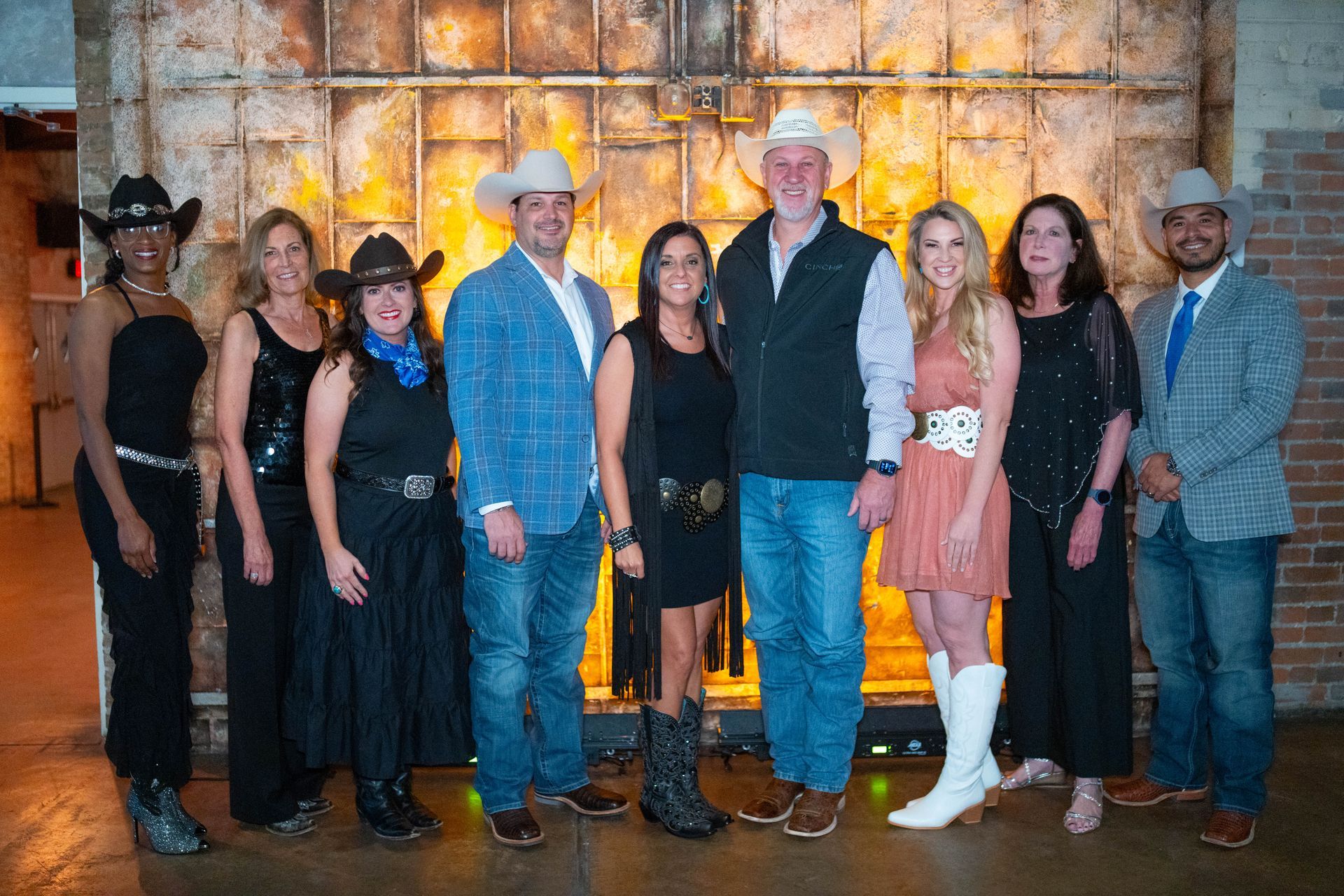 Group of people in cowboy attire, posing in front of a metal backdrop.