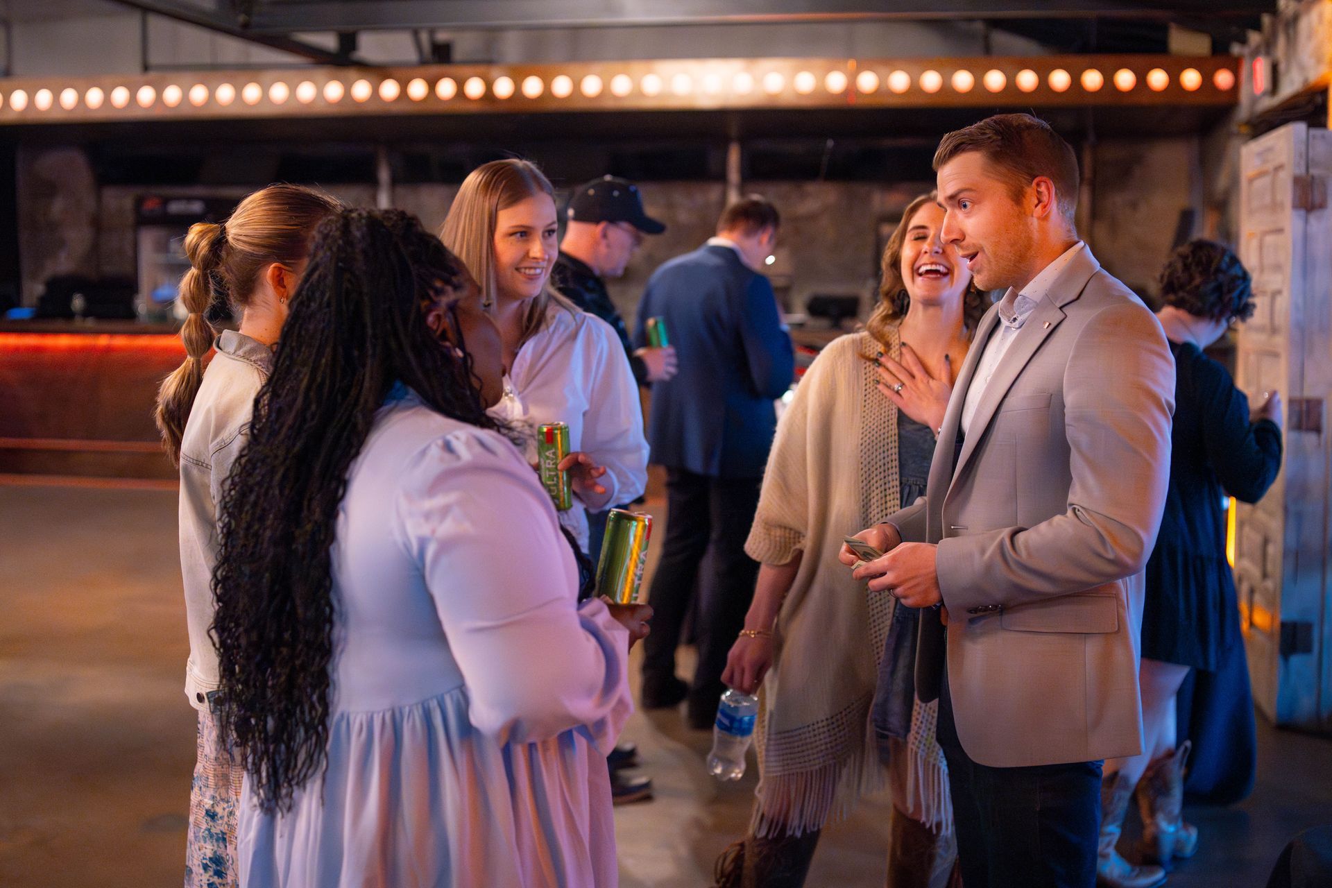 People socialize and laugh at an indoor event. Woman with long braids converses with others. Low lighting.