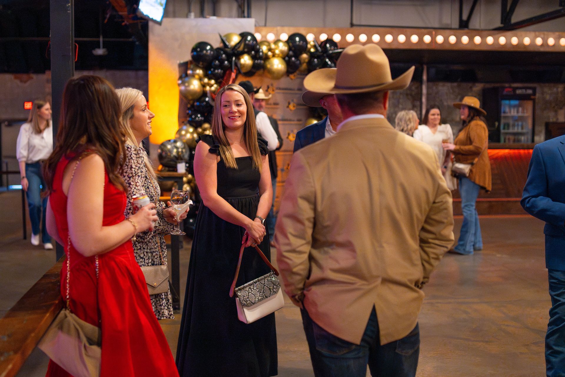 People in formal attire, including a woman in a red dress, at an event with decorations and a cowboy hat.